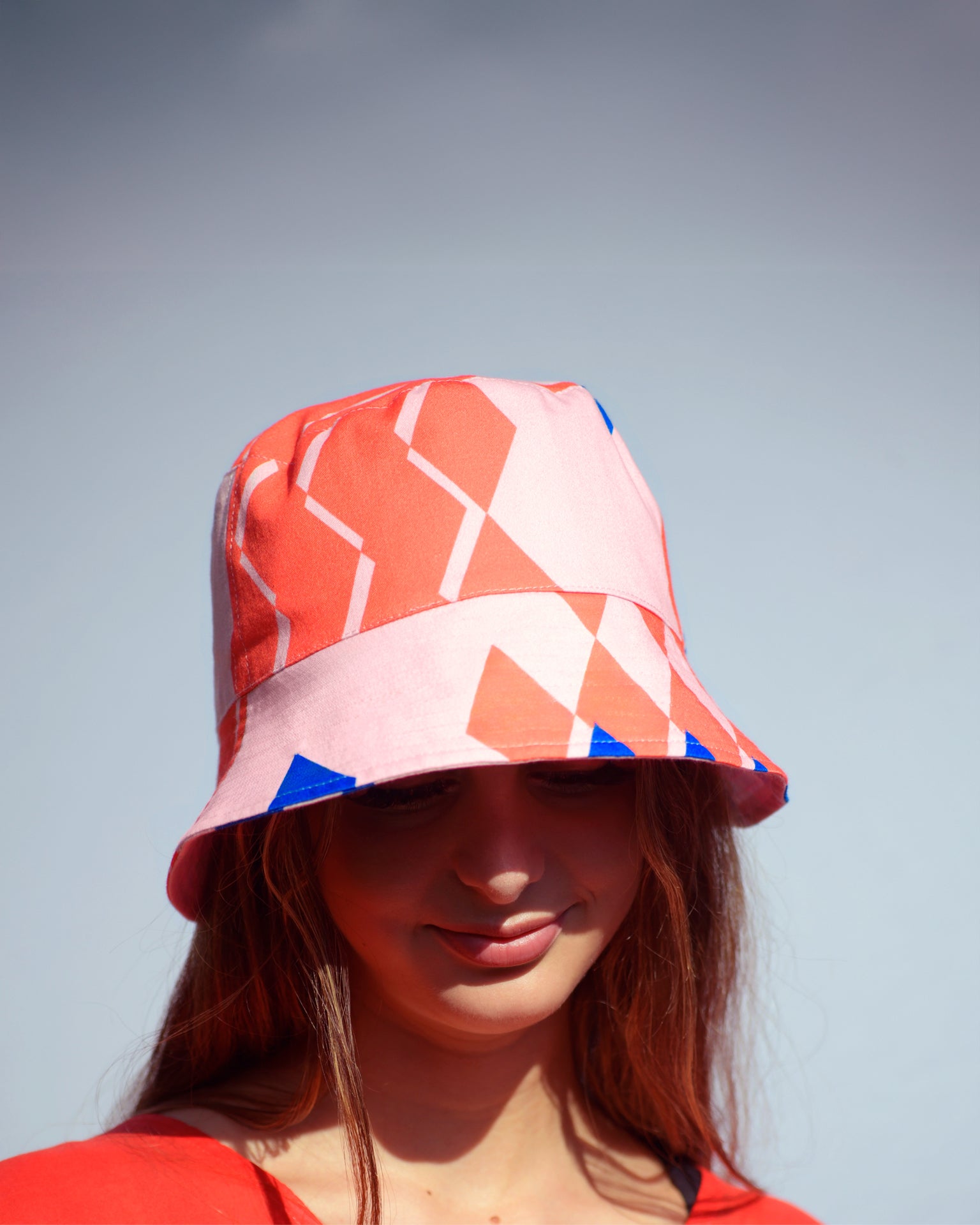 Young woman wearing a colorful geometric-patterned bucket hat against a clear sky.