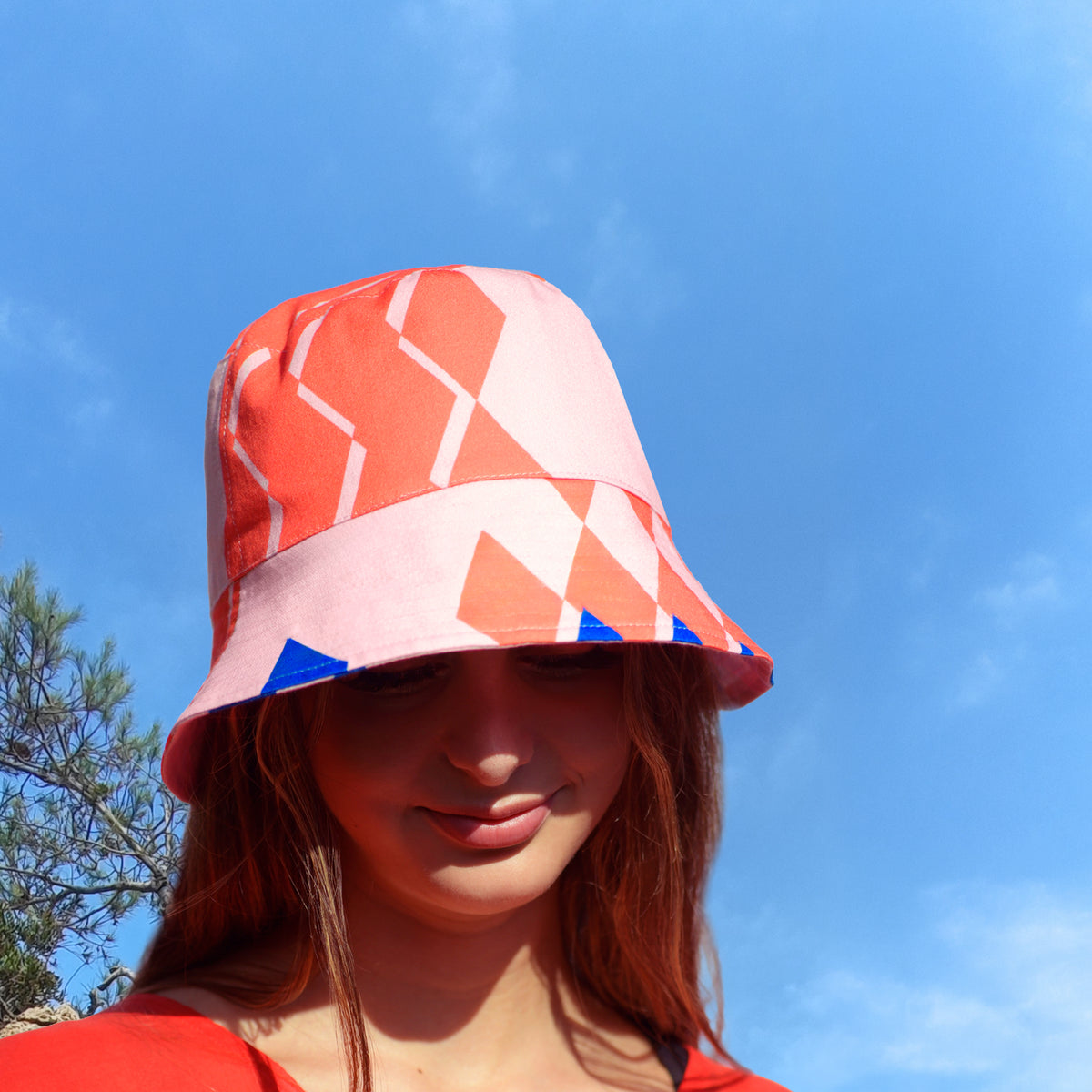Person wearing a printed bucket hat in blue, coral and pink against a blue sky.