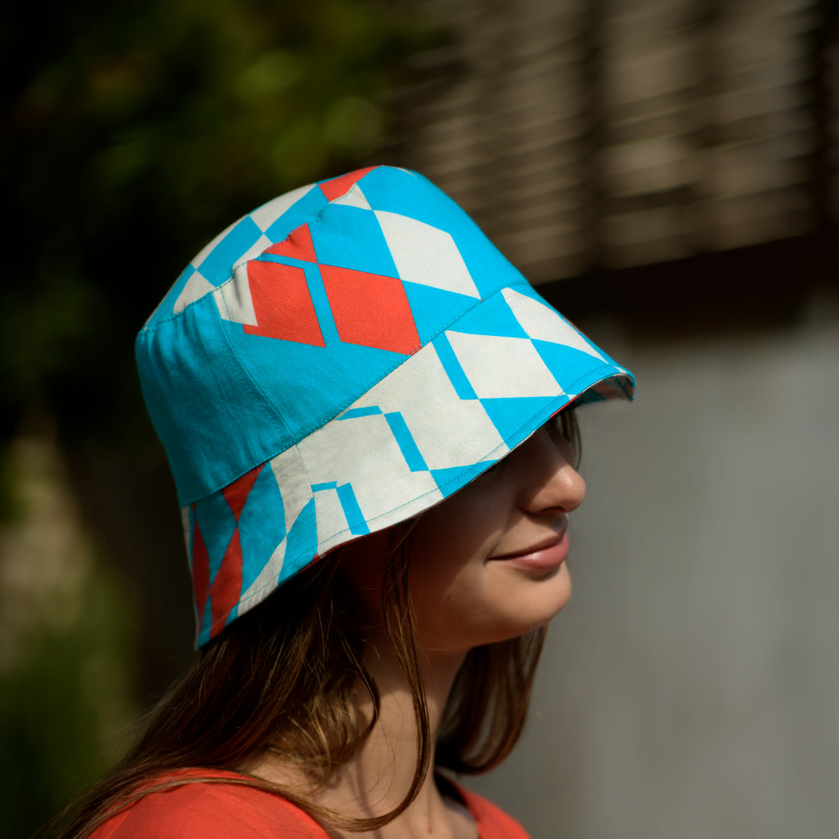 Person wearing a bucket hat with geometric pattern in turquoise, beige, and raspberry red outdoors