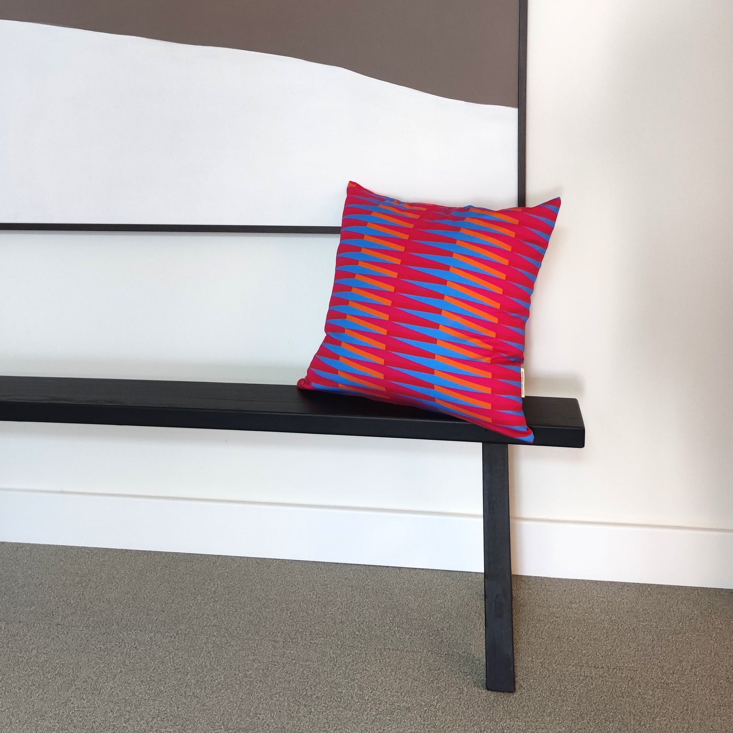 Black bench with a colorful printed Kristina Nordlöf pillow against a white wall