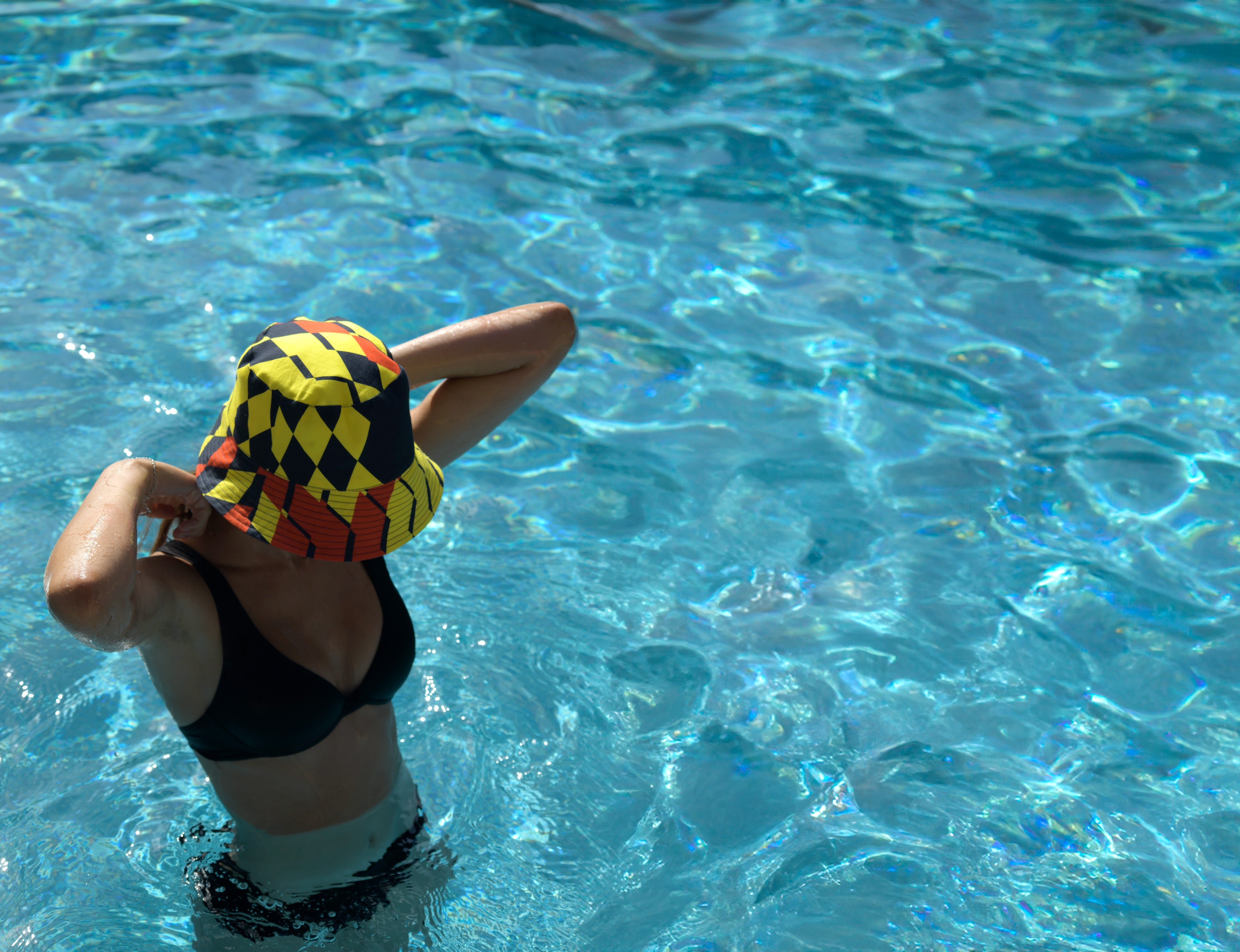 Young woman in a pool with the Kristina Nordöf bucket hat in dark gray, yellow and orange