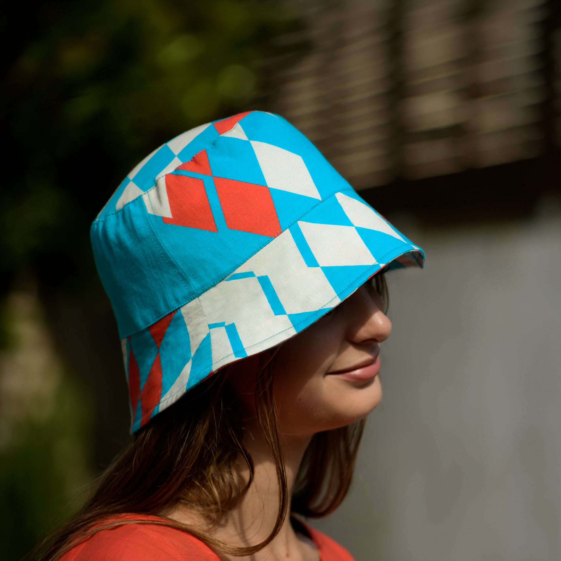 Person wearing a bucket hat with geometric pattern in turquoise, beige, and raspberry red outdoors